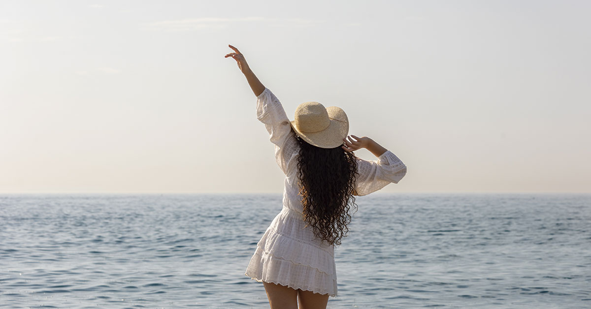 mujer con sombrero de paja disfrutando vistas del mar